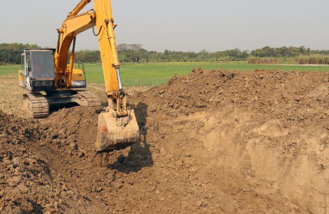 Excavator digging soil on rural farmland for drainage installation as part of Rural Drainage Solutions NSW. Excavator digging soil on rural farmland for drainage installation as part of Rural Drainage Solutions NSW.