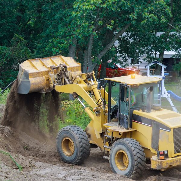 Front-end loader moving soil on a rural site near a house, part of earthmoving and excavation work by Rural Property Services NSW.