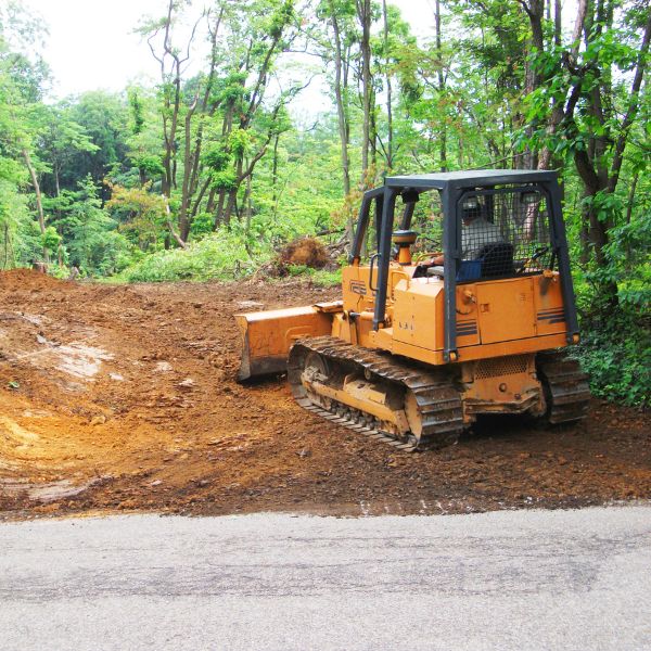 Grading soil at the entrance of a rural driveway, surrounded by trees and vegetation, by Rural Property Services NSW.