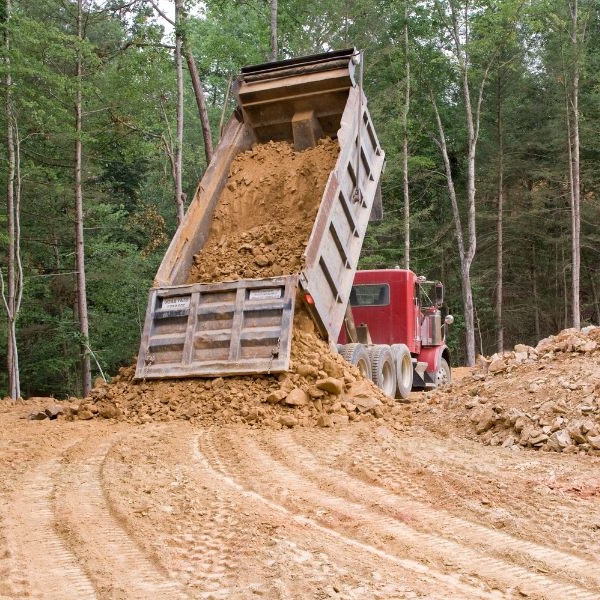 Red truck dumping fill for rural private road construction in a forested area by Rural Property Services NSW