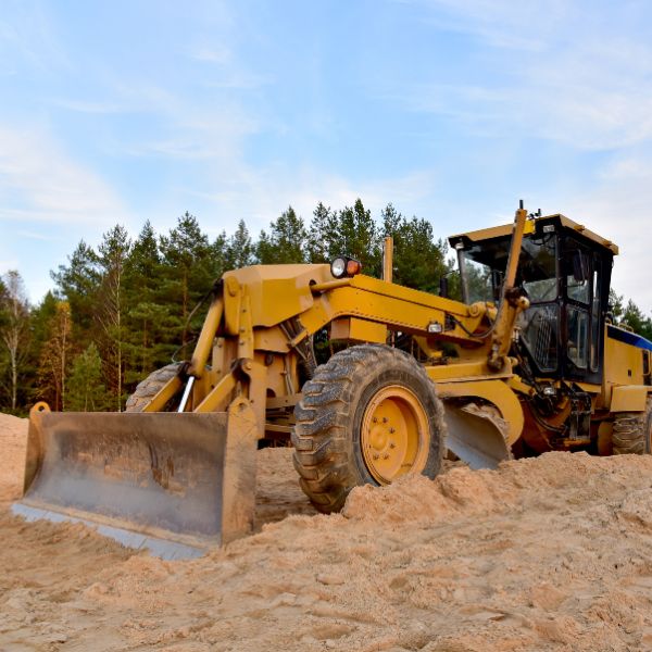 Road grader levelling sandy soil on a rural job site, part of Grading and Levelling services by Rural Property Services NSW