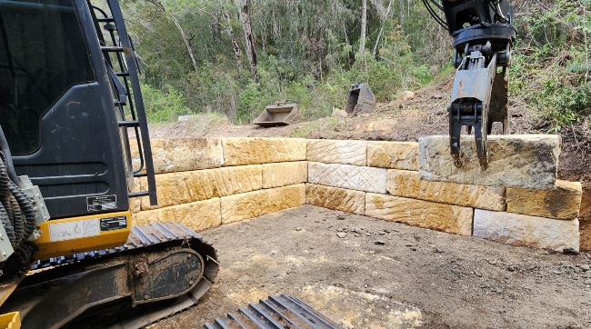 Rural Property Services NSW installing a sandstone retaining wall using excavator and grapple attachment Rural Property Services NSW installing a sandstone retaining wall using excavator and grapple attachment