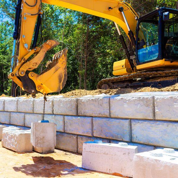Concrete retaining wall under construction with heavy machinery on a rural site, built for stability and erosion control by Rural Property Services NSW