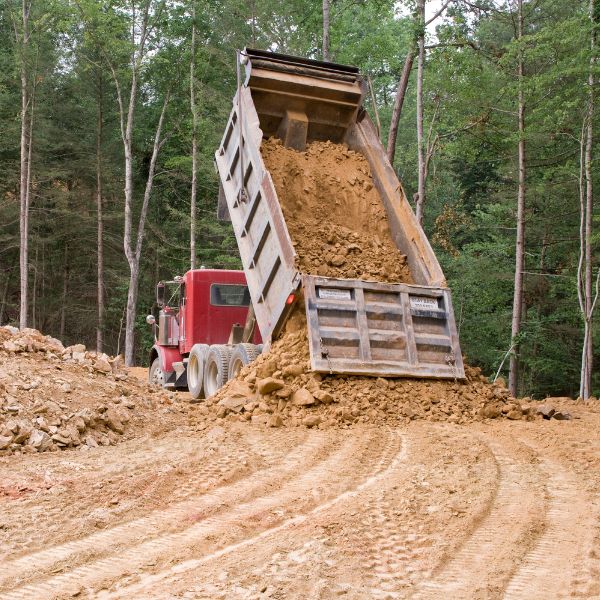 Tipper truck unloading soil during rural private road construction by Rural Property Services NSW, preparing a solid base through bushland